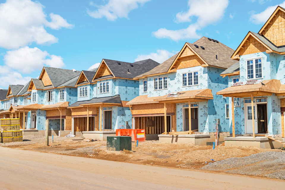 Homes under construction against a blue sky in a neighborhood.