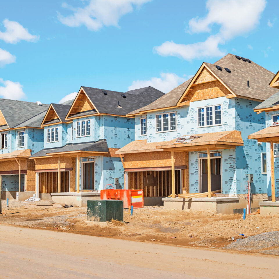 Homes under construction against a blue sky in a neighborhood.